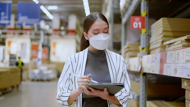 Portrait of asian woman business owner wear mask use tablet checking amount of stock product inventory on shelf at distribution warehouse factory.logistic business shipping and delivery service