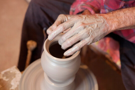 
Man's hands working with clay on pottery wheel