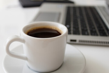 The concept of a workplace with coffee, a laptop and a notebook with a pen on a modern white office desk. Easy to use. Minimalism. Side view.