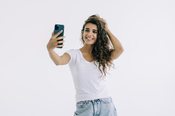 Fototapeta premium Smiling young woman making selfie photo while waving palm isolated on a white background
