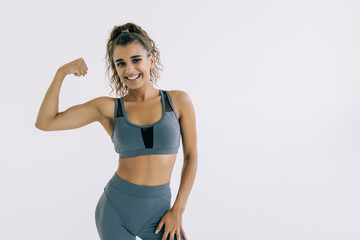 Fototapeta premium Cheerfully smiling sporty woman demonstrating biceps on white background
