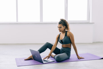 Fototapeta premium Young healthy woman meditating watching live online tv pilates class tutorial using laptop computer at home doing yoga virtual training fitness workout meditation exercise in apartment.