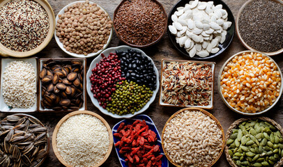 Collection of dry organic colorful cereal and grain seeds in wooden bowl in dark tone, consisted of bean, flax seed, goji berry, rice, peanut, job's tear, mung, and corn