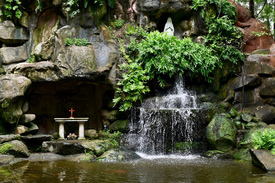 Statue of Our lady of grace virgin Mary view with natural background in Waterfall flows down from the rock cave at Thailand.