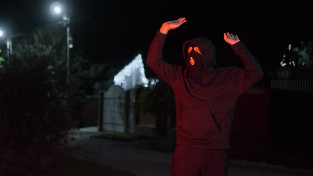 Thief in a mask carries a stolen TV late at night, is caught by the police with flashing lights, funny raises his hands up and drops the TV, concept of security and violation of the law