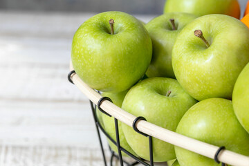basket with green apples on a light wooden table close-up, healthy food and diet concept, place for text