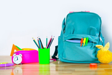 funny school backpack with markers, bright pencil case, fluffy keychain glass with colored pencils and an alarm clock on a wooden table. back to school concept.