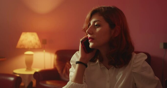 Giovane ragazza italiana parla al telefono seduta sul divano di casa