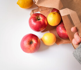 Naklejka na ściany i meble recycling, shopping and ecology concept - hand holding paper bag with apples ans lemons on table