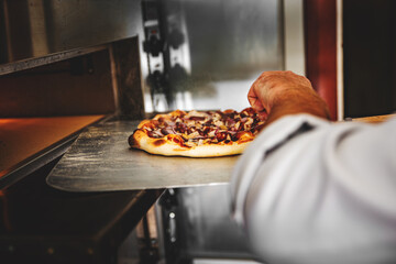 Closeup hand of chef baker making pizza at kitchen. Put on landing shovel and send it to the oven.