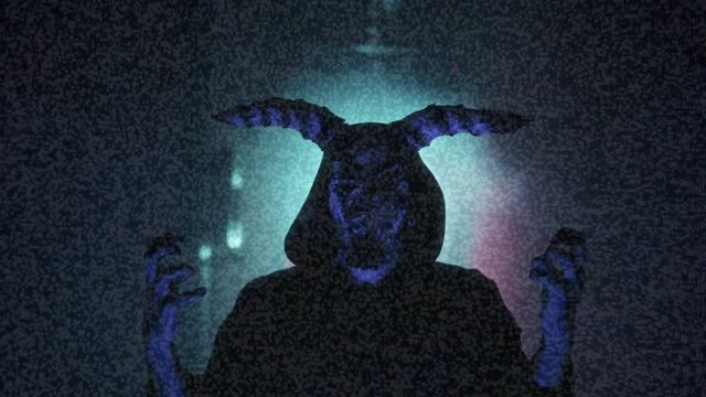 Old tv screen showing devil with glitch effect close-up. Exorcist with horns putting hands up, standing in dark corridor, horror film concept. Haunted house movie, video clip with ghost. 