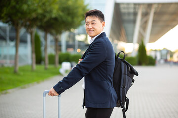 Happy Asian tourist with a big suitcase near the airport, at a business meeting arrives looking at...