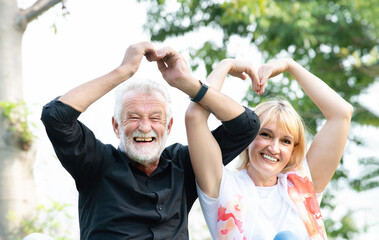 Portrait of senior caucasian couple making heart shape together in the park. Happy elderly couple in a summer park. Cheerful retired couple outdoors. Mature couple in spring park