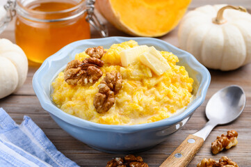 Rice milk pumpkin porridge with walnuts, butter and honey in a blue bowl on a wooden table. Healthy food. Selective focus