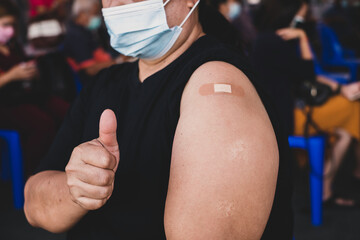 Fat woman hand showing thumbs up has gone to vaccinate coronavirus covid19 shoulder with bandage on orange background, Healthcare And Inoculation Concept