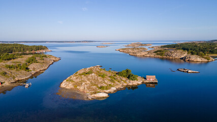 Naklejka na ściany i meble Swedish archipelago in Bohuslän with a small house on an island and a blue sky - Drone Perspective Landscape Photography