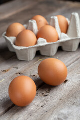Brown eggs in a cardboard box. Eggs are scattered over a wooden background. Healthy food concept.