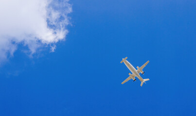 Small twin-engine turboprop business aircraft flying under blue sky viewed from below. Bottom view of airplane flying on bright sky background with clouds