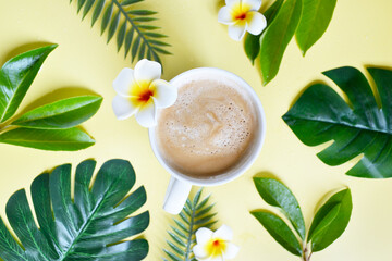 Cup of coffee with tropical leaves on the yellow background. Coffee latte with plumeria in the...