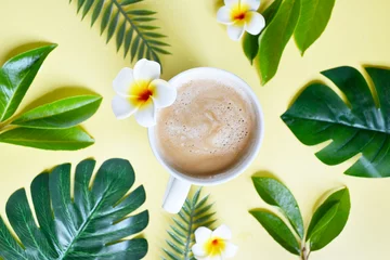 Foto auf Leinwand Cup of coffee with tropical leaves on the yellow background. Coffee latte with plumeria in the middle of the table. Coffee break on exotic, tropical island. Happy day, morning. Enjoying vacation.   © Maryna