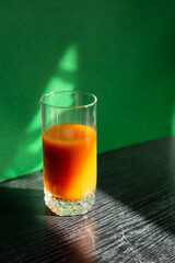 Orange vitamin citrus juice in glass. Trendy shadow and light. Creative healthy food photo. Sunlight on black kitchen table and green wall.