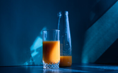 Blue night light on kitchen. Orange vitamin citrus juice in glass and glass bottle. Trendy shadow and light.Creative healthy food.