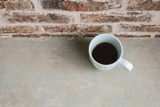 White coffee mug with black coffee outside on concrete patio with brick wall