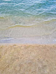 A vertical photo with a top view of clear turquoise river water and light brown sand on the banks of the river. Water splashes against the shore. The texture of sand and moving water.
