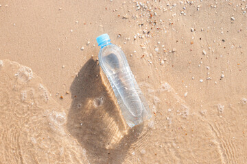Plastic water bottle on the beach is washed by a wave. Top view, flat lay