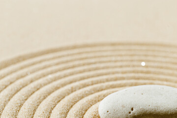 Fototapeta na wymiar Aesthetic minimal background with zen stone on sand. Japanese Zen Garden with concentric circles around stone cairn.
