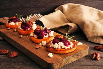 Autumn sweet potato crostini appetizers with cheese, cranberries and pecans on a wood platter....