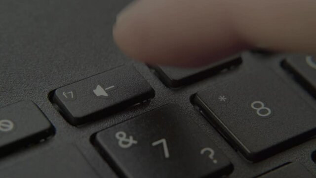 The finger presses the Mute button on the keyboard.
