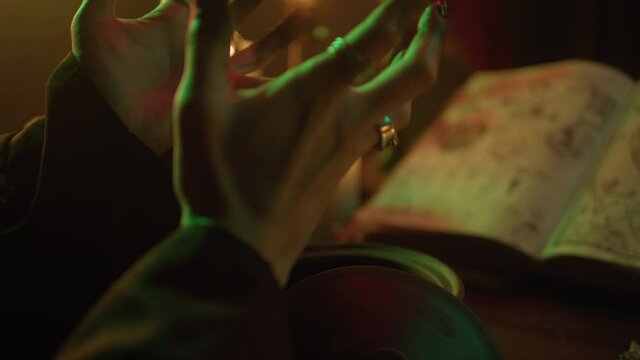 Witch cooking potion elixir close-up. Table with spellbook for making rite. Herbs, burning candles, crystal magic ball for sacrifice. Halloween theme, full moon, witchcraft. 