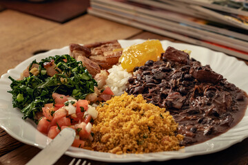 Prato feito de feijoada e acompanhamentos, arroz, vinagrete, couve, panceta e um pedaço de laranja