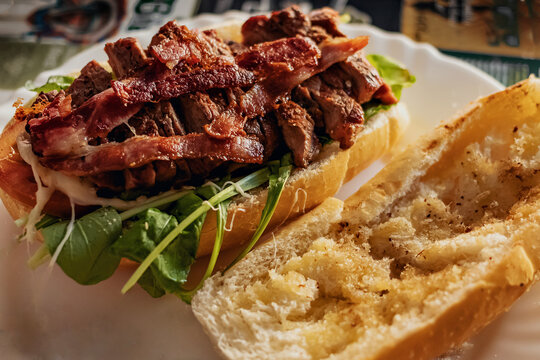 Sandu&iacute;che de carne e bacon com salada de r&uacute;cula exibindo o receio num prato em uma mesa de bar