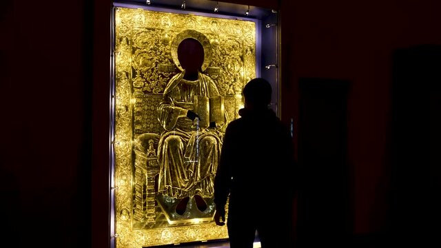 Rear view of a man coming close to the sacred golden icon under the protective glass. Concept. Interior of the orthodox church dark hall.