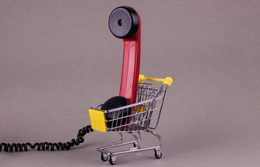 Red receiver from old rotary telephone in small shopping cart on gray background