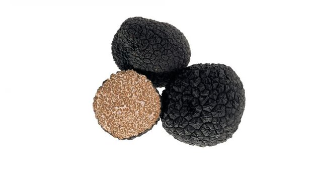 Top view of two whole and one halved black truffle mushrooms rotating. Isolated on white background.