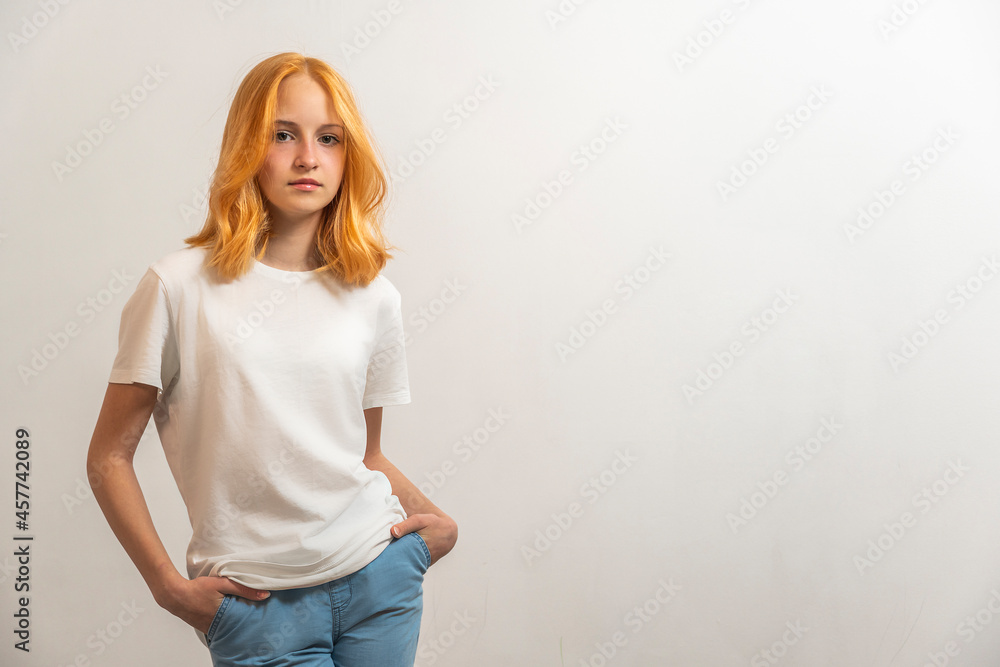 Wall mural Portrait of a teenage girl with red hair and a white T-shirt on a light background