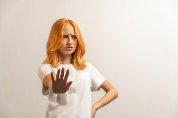 Portrait of a teenage girl with red hair and a white T-shirt say no on a light background