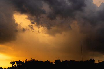 A picture of a rain cloud with a lot of noise, a photograph of a falling rainstorm, a large storm cloud over a shadowy forest. Clouds and evening sunlight. This picture has a lot of noise.