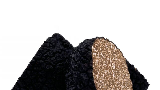 Closeup of black truffle mushroom halves rotating on white background.