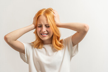 Fototapeta premium Portrait of a teenage girl with red hair and a white T-shirt to fear on a light background