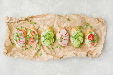 Various vegetarian sandwiches with vegetables and herbs on parchment on a light table. Proper nutrition. Diet food. Food background. View from above. Copy space.