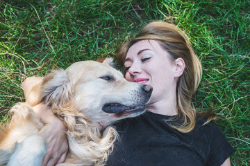 A young blonde woman lies on the grass with her dog.