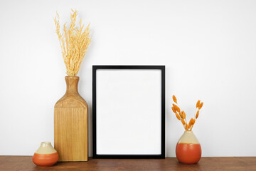 Mock up black frame with autumn branches and decor on a wood shelf. Fall concept. Portrait frame against a white wall.