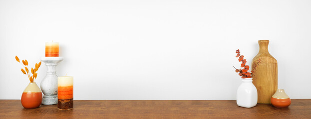 Autumn decor on a wood shelf against a white wall background. Banner with copy space. Candles, vases and vibrant branches.