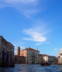 Venice, Italy - Grand Canal with blue sky and wispy clouds.  Palaces line the banks of the canal, and a speedboat navigates the center of the waterway. Vertical with modern colors.
