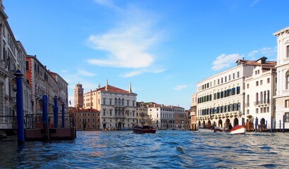Venice, Italy - Grand Canal with blue sky and wispy clouds.  Palaces line the banks of the canal, and a speedboat navigates the center of the waterway. Horizontal with modern colors.