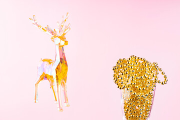 Toy deer and Christmas beads in a champagne glass on a pink background. Christmas composition with holographic toy deer. Festive holiday concept. Copy space